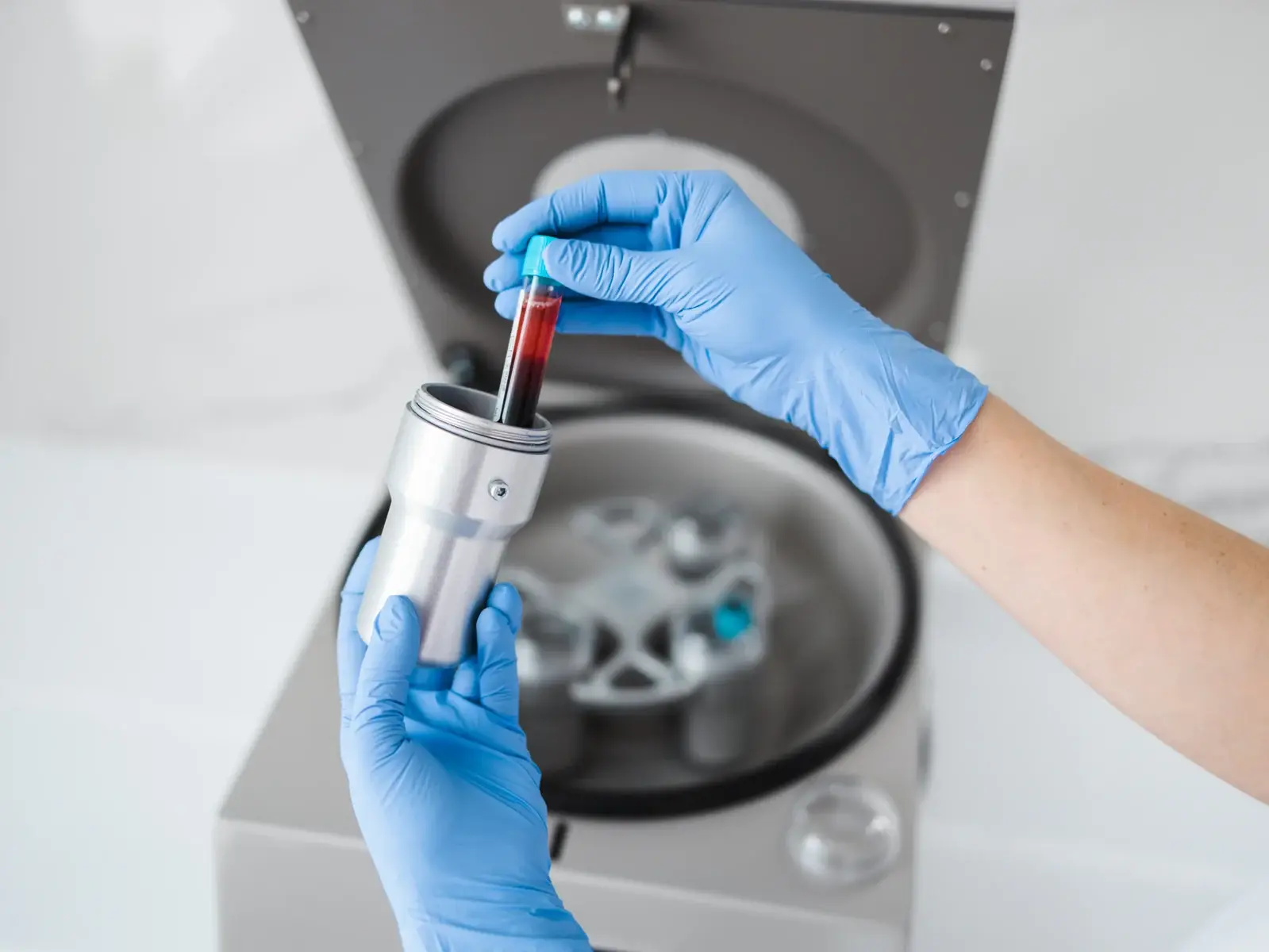 A clinician in blue gloves loading a tube of drawn blood into a centrifuge in South Tempe, AZ