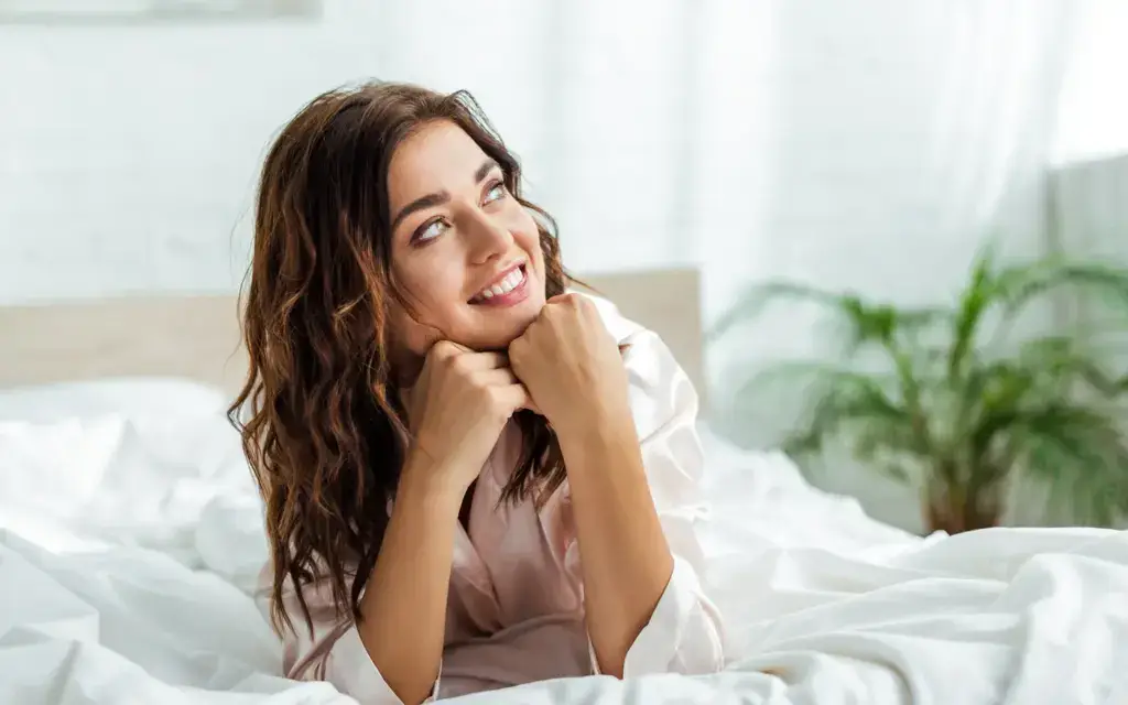 Smiling woman relaxing in bed in morning light, O-Shot sexual wellness care in South Tempe, AZ